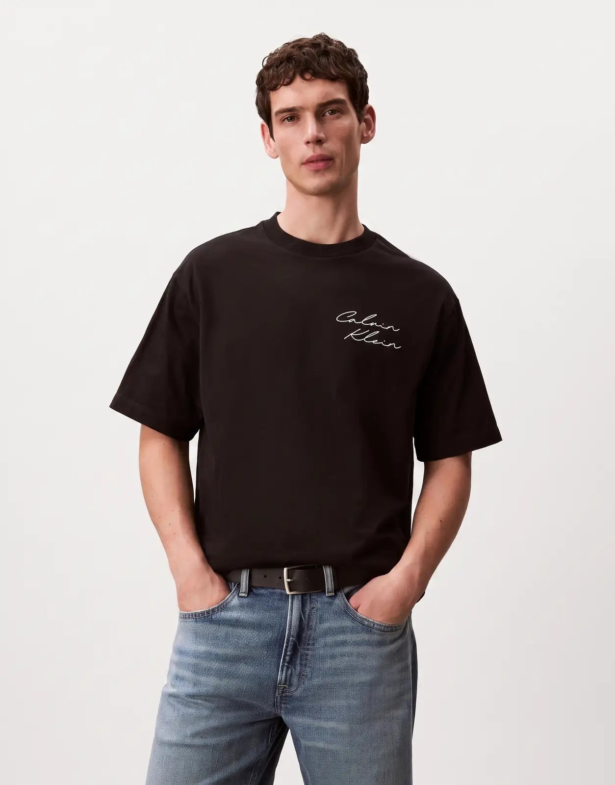 A male model poses in a black Calvin Klein 16s April Graphic Seasonal Fashion t-shirt featuring a white script logo.