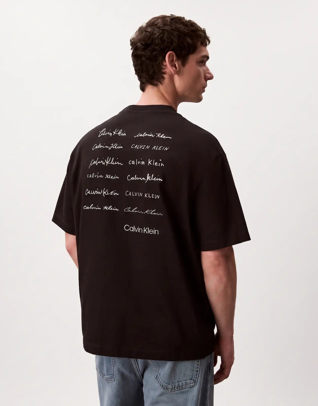 Black Calvin Klein 16s April Graphic Seasonal Fashion t-shirt with multiple Calvin Klein logo prints on the back, worn by a