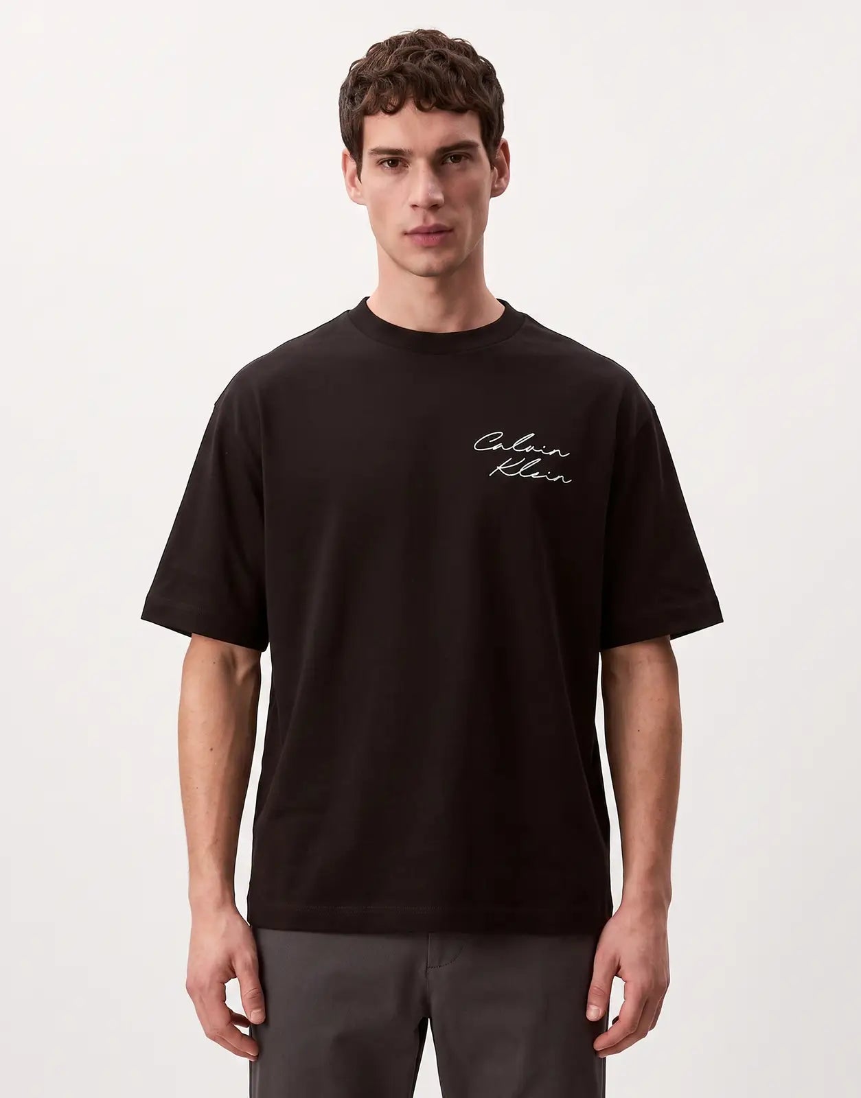 A Calvin Klein 16s April Graphic Seasonal Fashion t-shirt in black with a white script logo, worn by a male model.