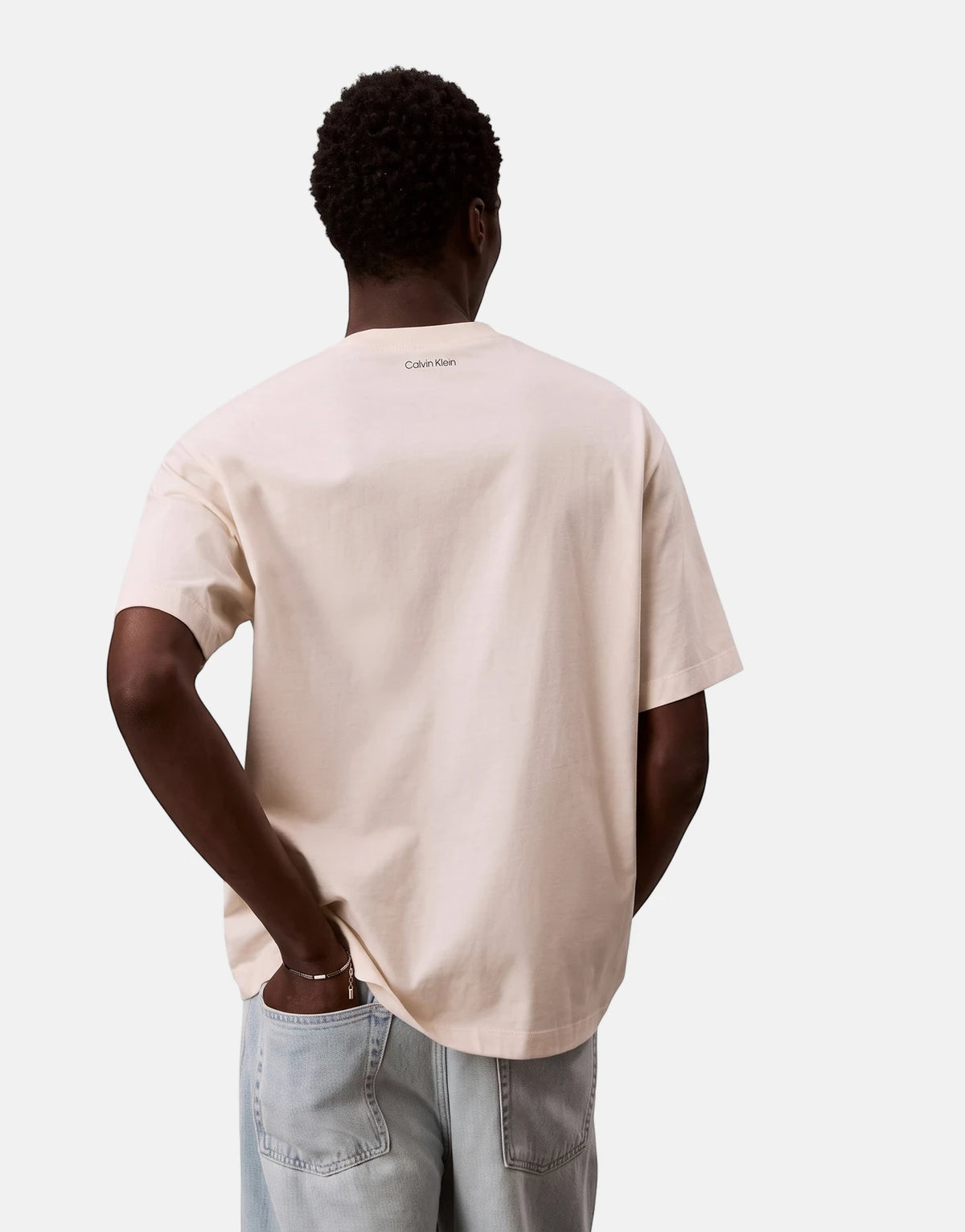 Back view of a male model wearing an oversized cream Calvin Klein 16s April Graphic Seasonal Fashion White T-Shirt and light
