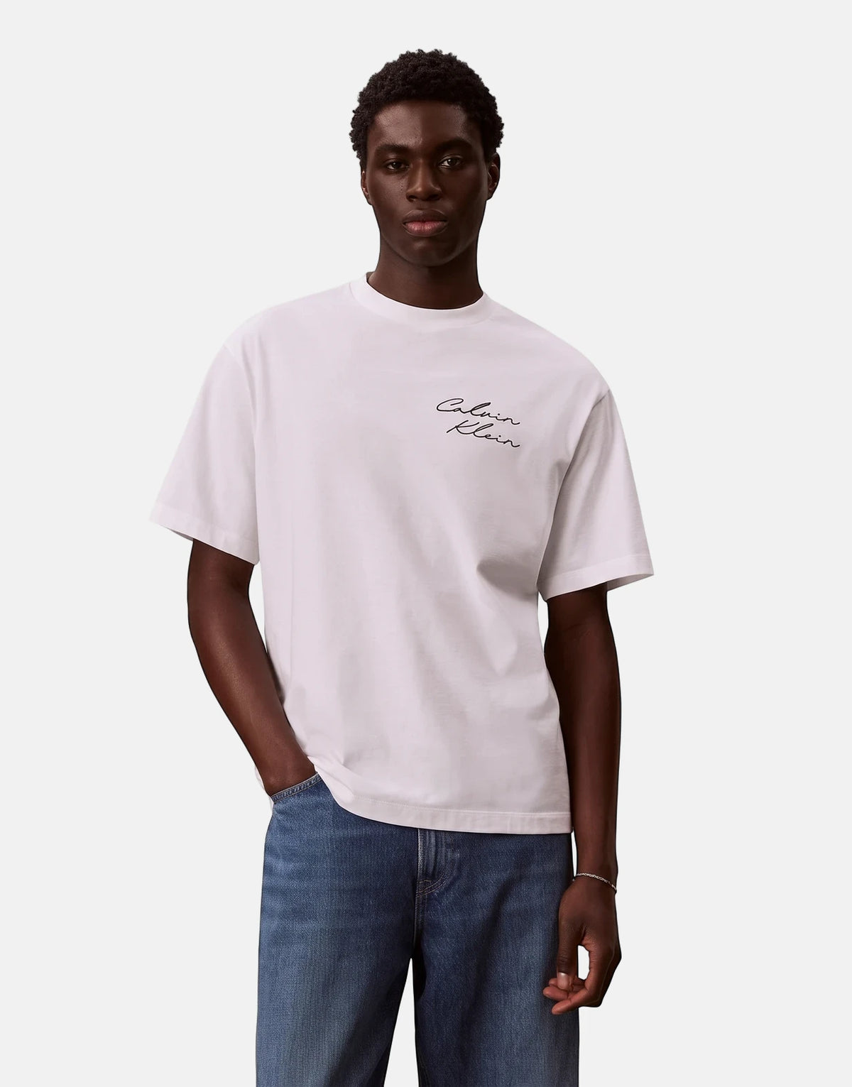 A dark-skinned male model wears a white Calvin Klein 16s April Graphic Seasonal Fashion T-shirt and blue jeans, posing