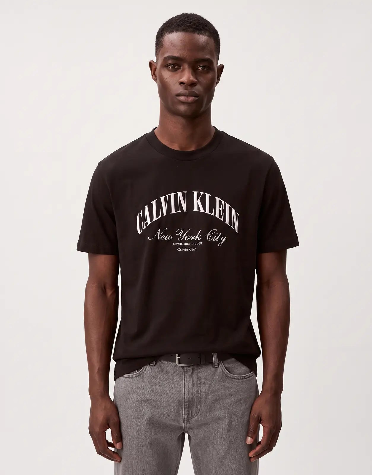 A men's black Calvin Klein 20s March Graphic T-Shirt with white arched 'CALVIN KLEIN' and 'New York City' script print on
