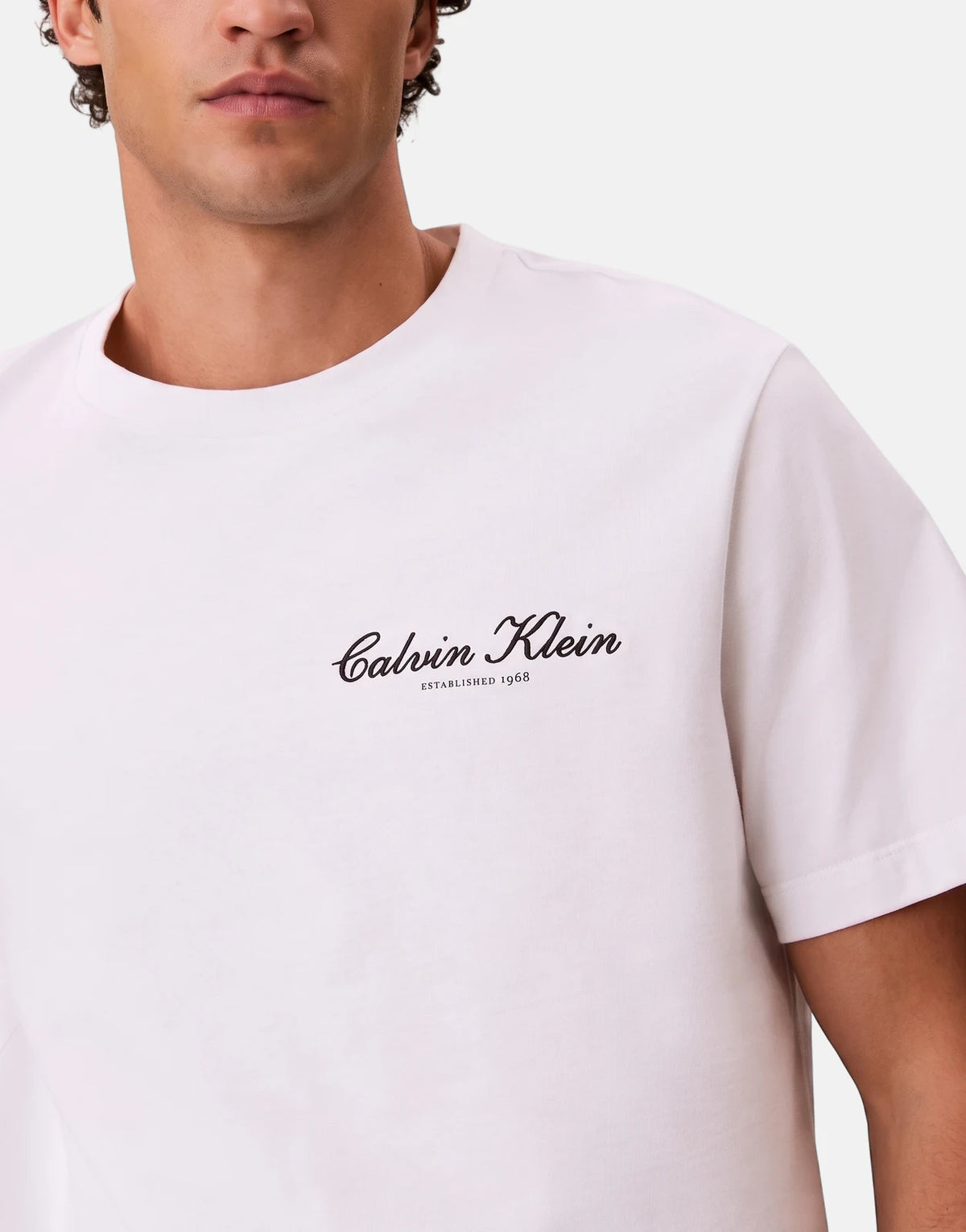 Close-up of a man wearing a white Calvin Klein t-shirt with the 'Calvin Klein ESTABLISHED 1968' logo on the chest.