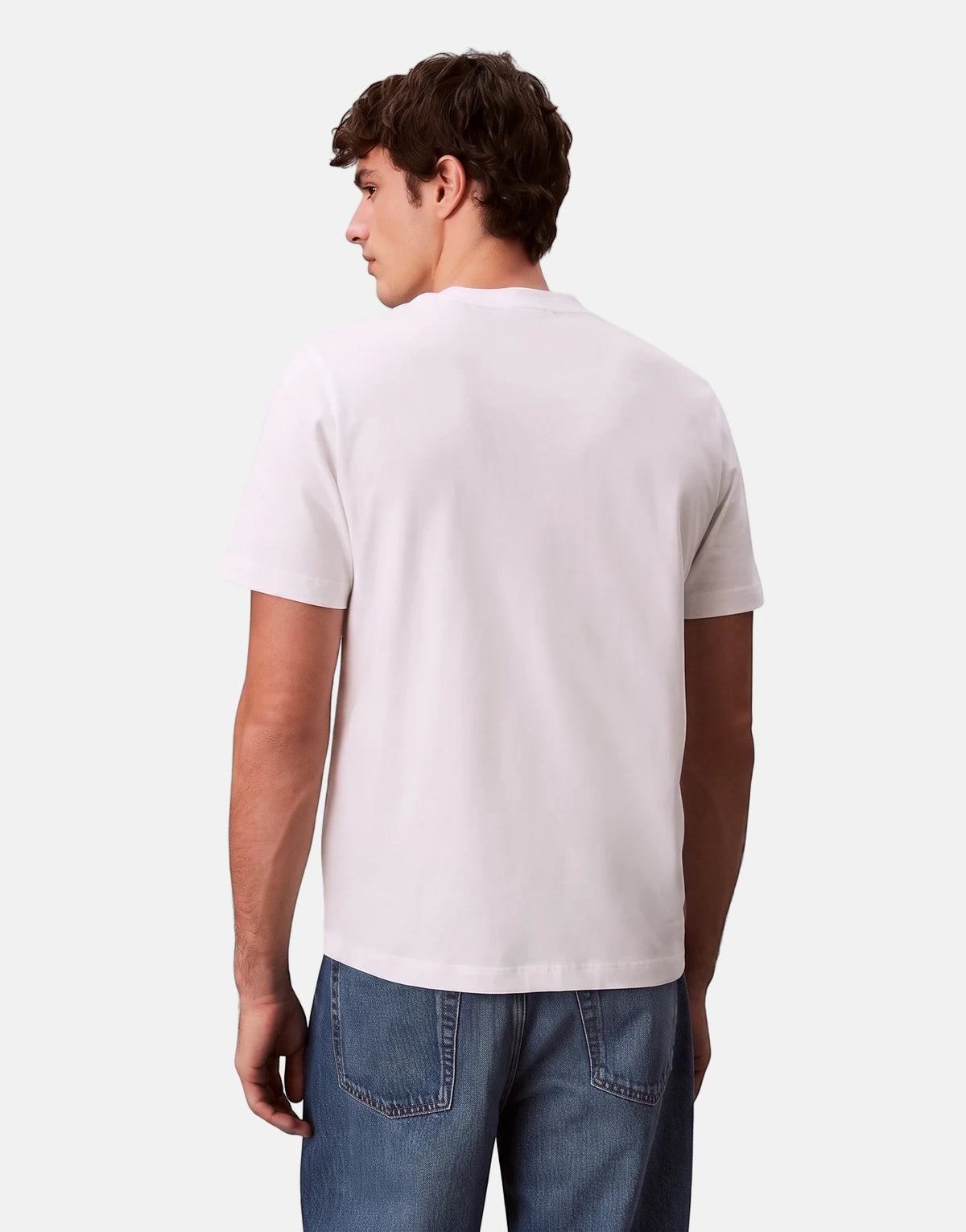 Man wearing a Calvin Klein 20s March Graphic Seasonal White T-Shirt and blue jeans, viewed from the back.