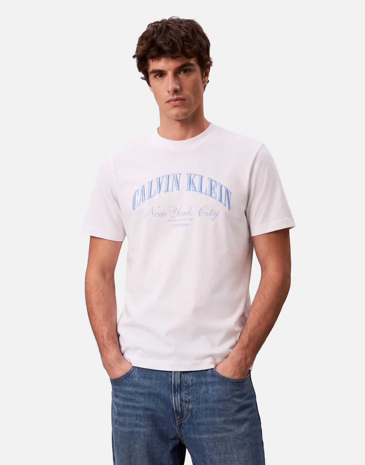 Male model wearing a Calvin Klein 20s March Graphic Seasonal white t-shirt and blue denim jeans.
