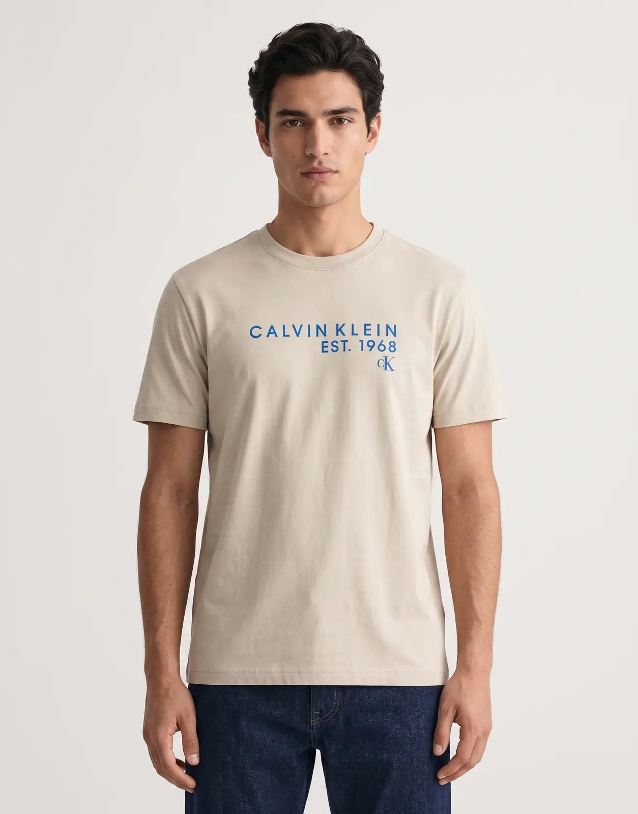 Calvin Klein 30s Wholesale Graphic Beige T-Shirt with a blue 'CALVIN KLEIN EST. 1968' and 'CK' logo print on the front, laid