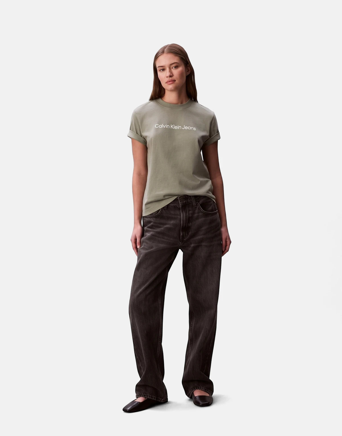 Female model wearing a Calvin Klein short sleeve logo t-shirt in grey paired with dark wide-leg jeans and ballet flats.