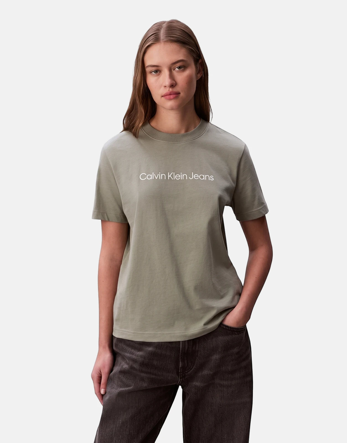 Female model wearing a Calvin Klein A-Inst Logo Classic T-Shirt in olive grey with dark wash jeans, hands in pockets.