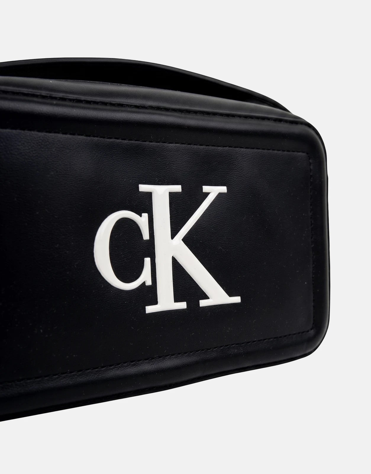 Close-up of a Calvin Klein Bold CK black camera bag featuring the prominent white 'CK' logo on the front, showing the