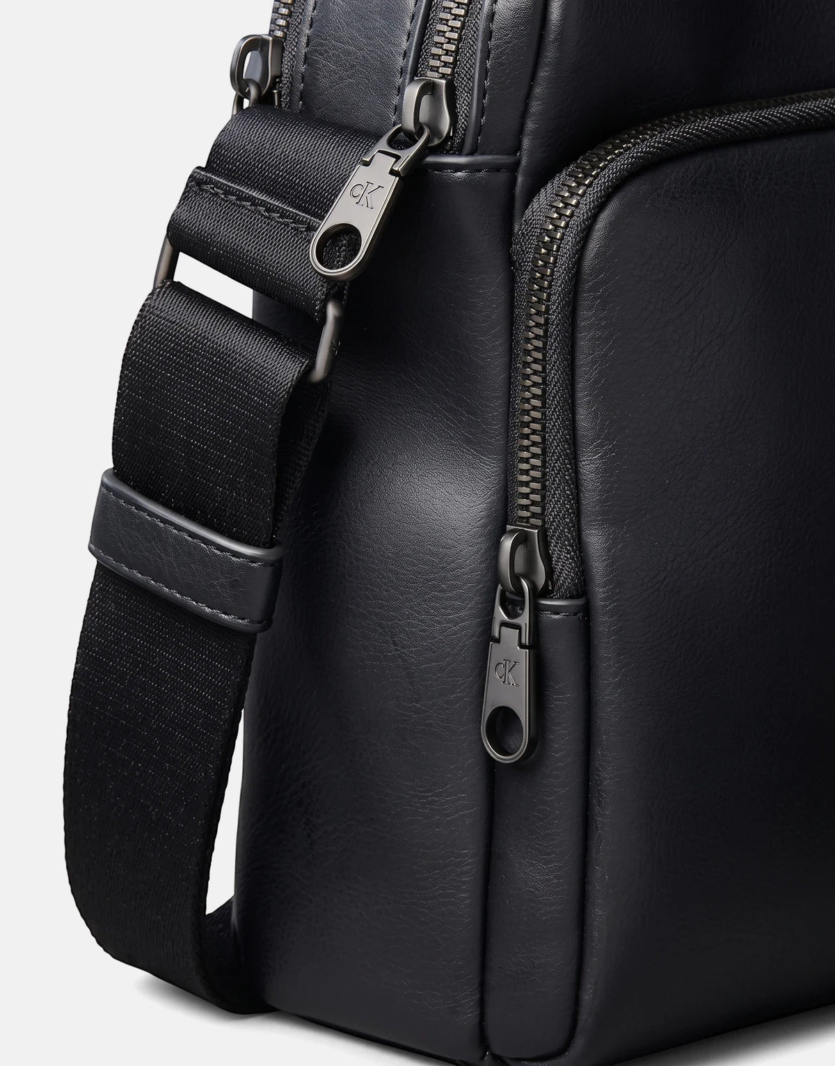 Close-up of a black Calvin Klein Bold CK Pocket Reporter bag, showing the textured material, black strap, and gunmetal CK