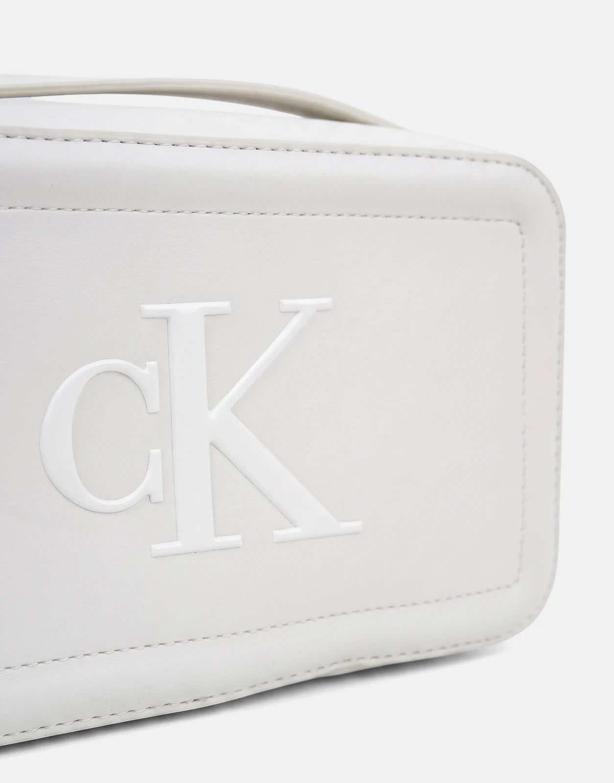 Close-up of a white Calvin Klein Bold CK camera bag, featuring the embossed CK logo on the front and visible stitching