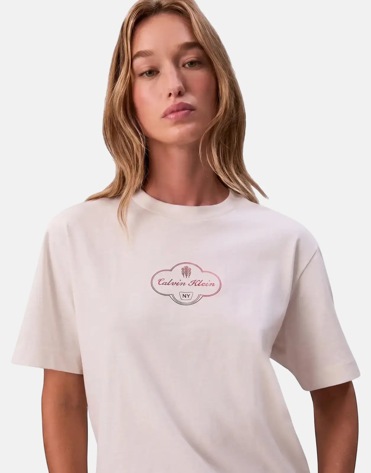 A female model wearing a white Calvin Klein Boxy Cocktail Logo t-shirt with a round neck and short sleeves.
