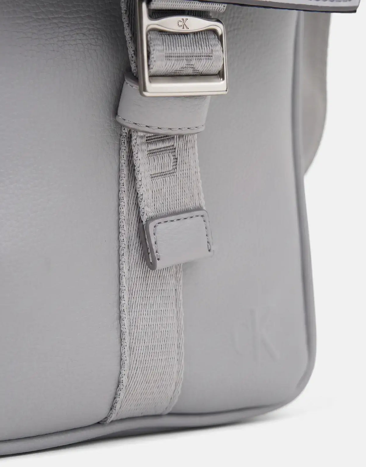 Close-up view of a grey textured Calvin Klein Cargo Flap Reporter Bag, showcasing the silver buckle and embossed logo.