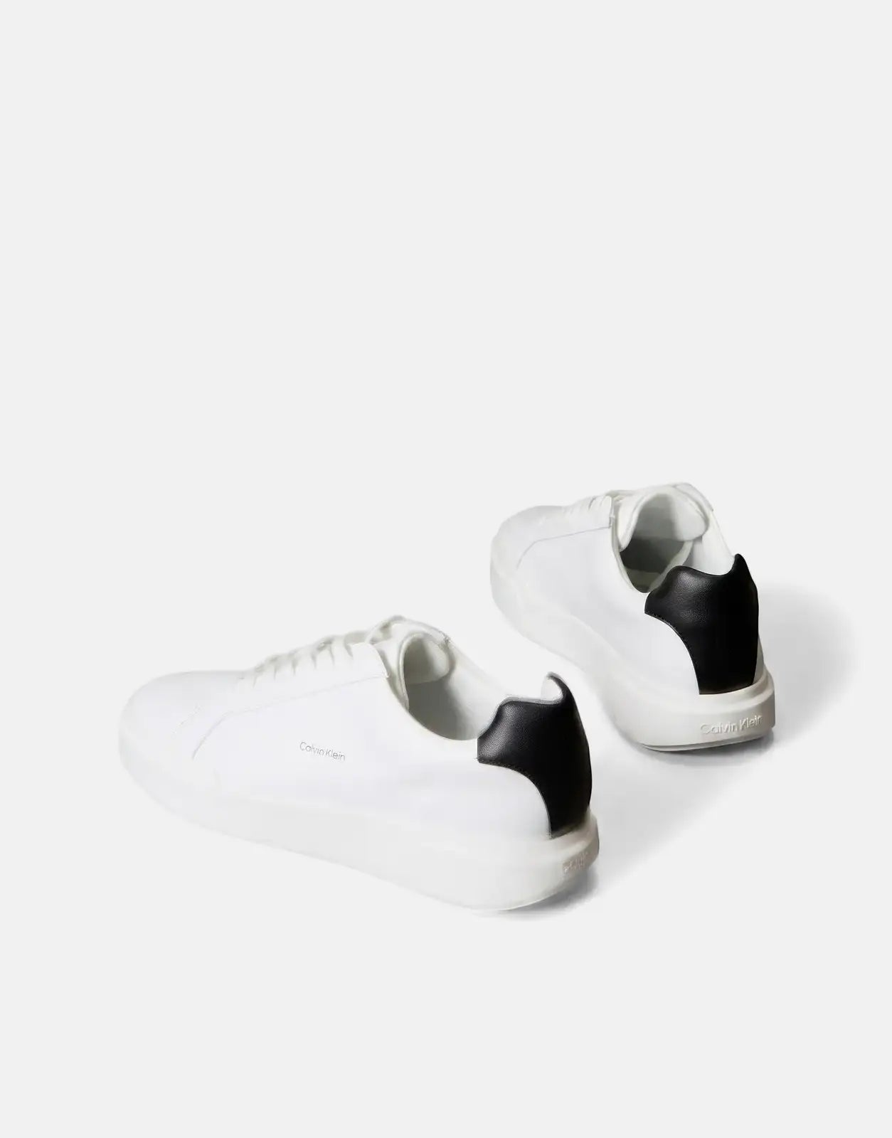 A pair of white and black Calvin Klein Chunky Cupsole sneakers in a three-quarter rear view on a gray background.