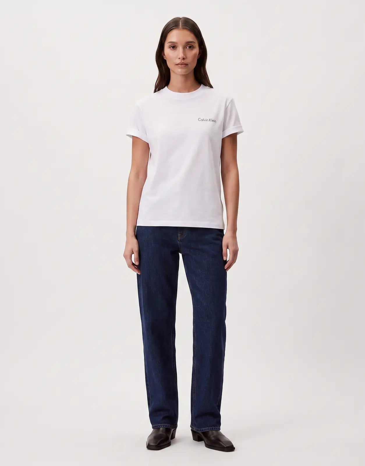 A female model wears a Calvin Klein Classic Graphic White T-Shirt with a subtle script logo, paired with dark jeans.