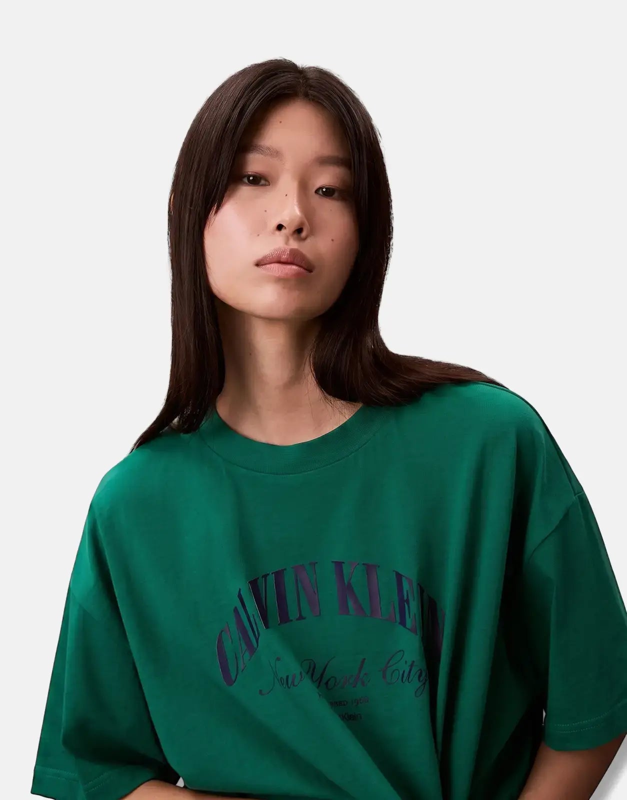 Young woman wearing a Calvin Klein Cropped Boxy Heritage Crest Logo Green T-Shirt, captured from the chest up.