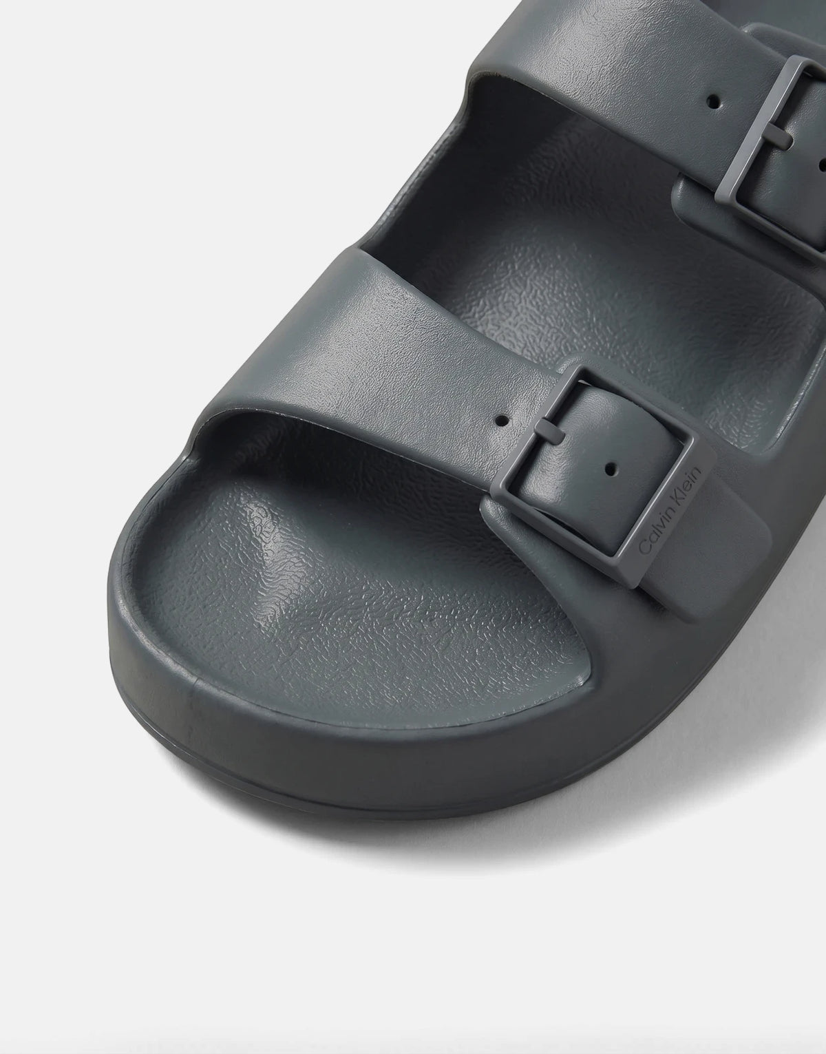 Close-up of a blue/grey Calvin Klein Ergon EVA double bar sandal with adjustable buckles on a flat surface.
