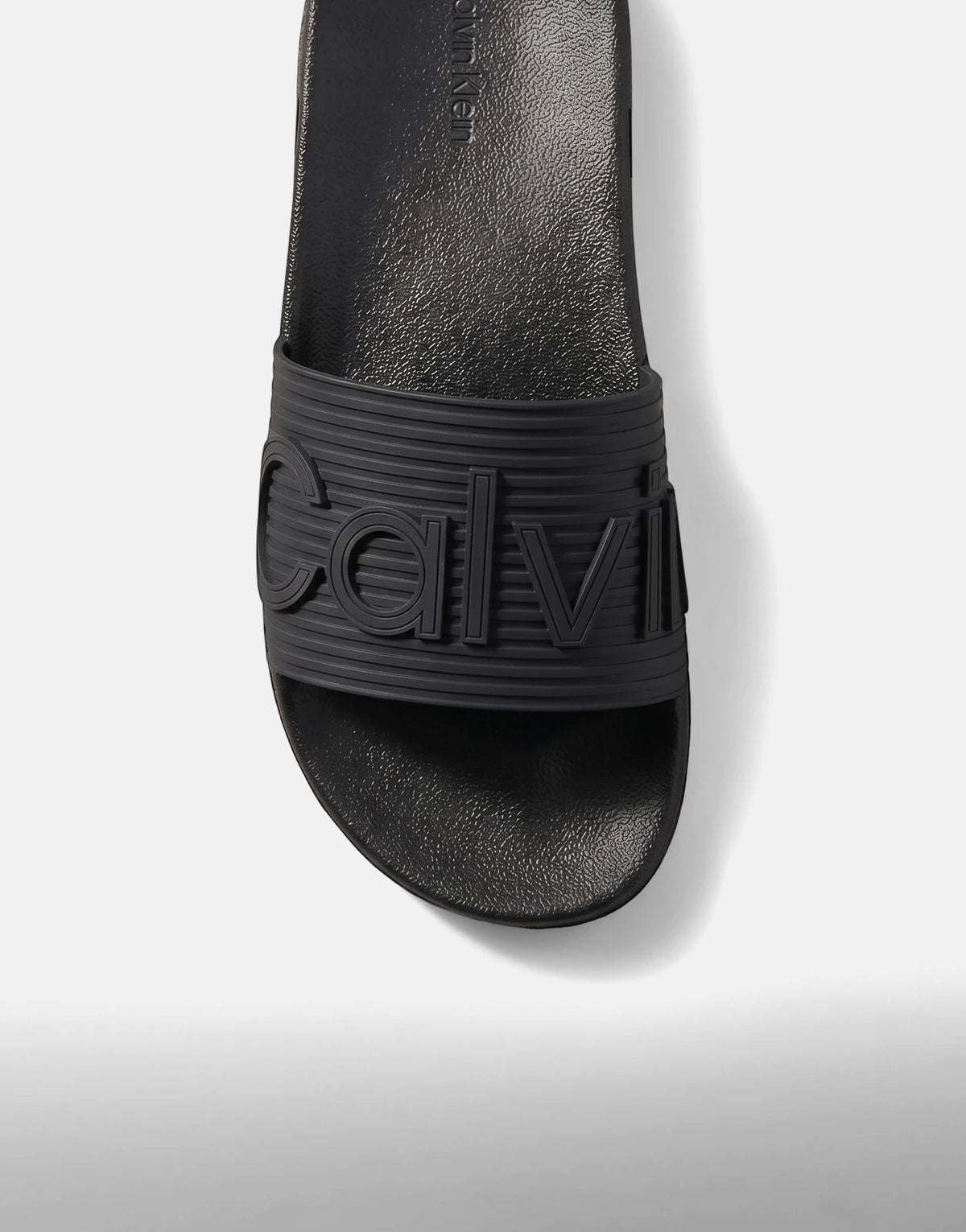 Close-up view of a single black Calvin Klein Essential Texture slide, featuring a ribbed strap with embossed branding.