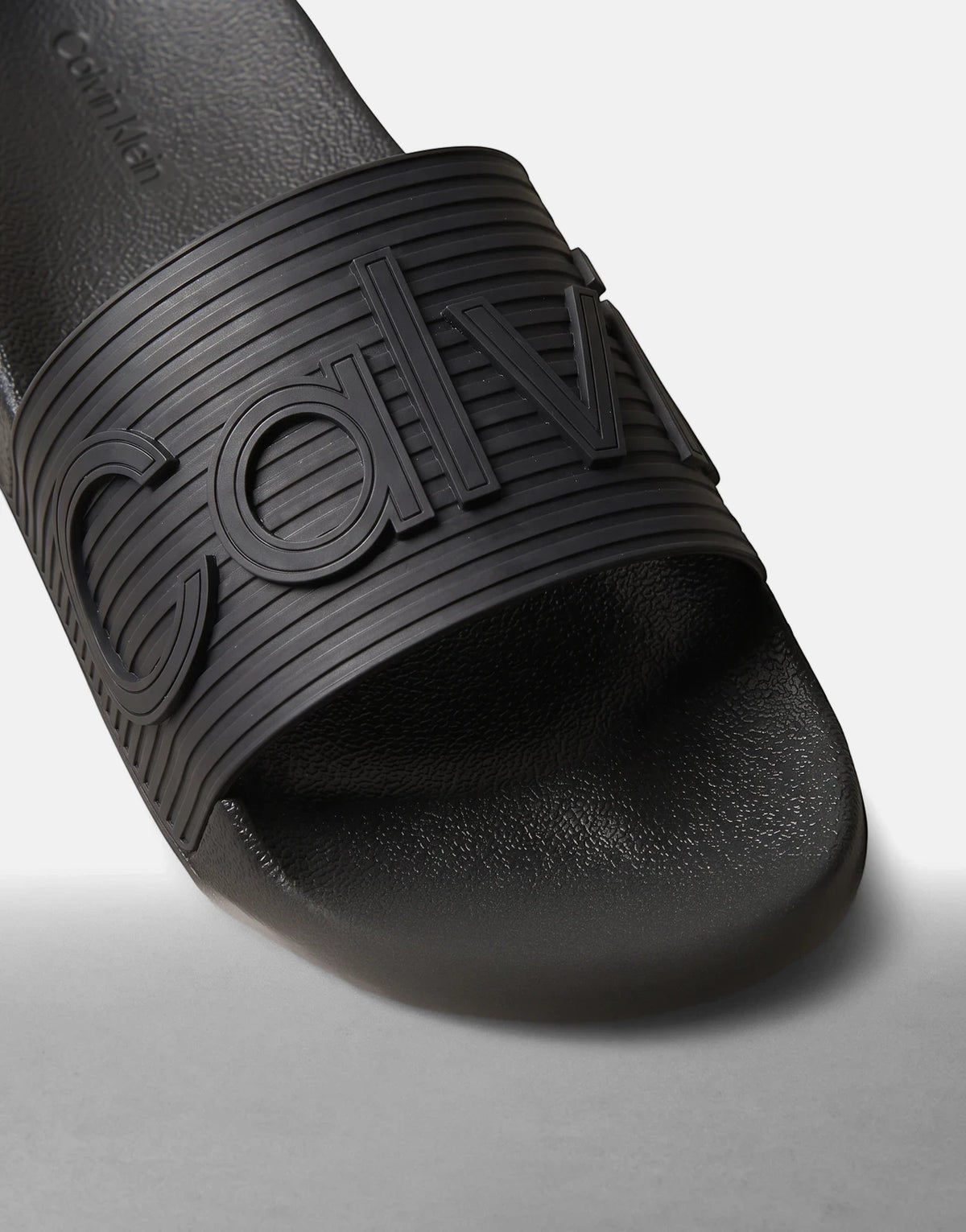 Calvin Klein Essential Texture slides in black, featuring a textured strap and a smooth footbed, angled view.