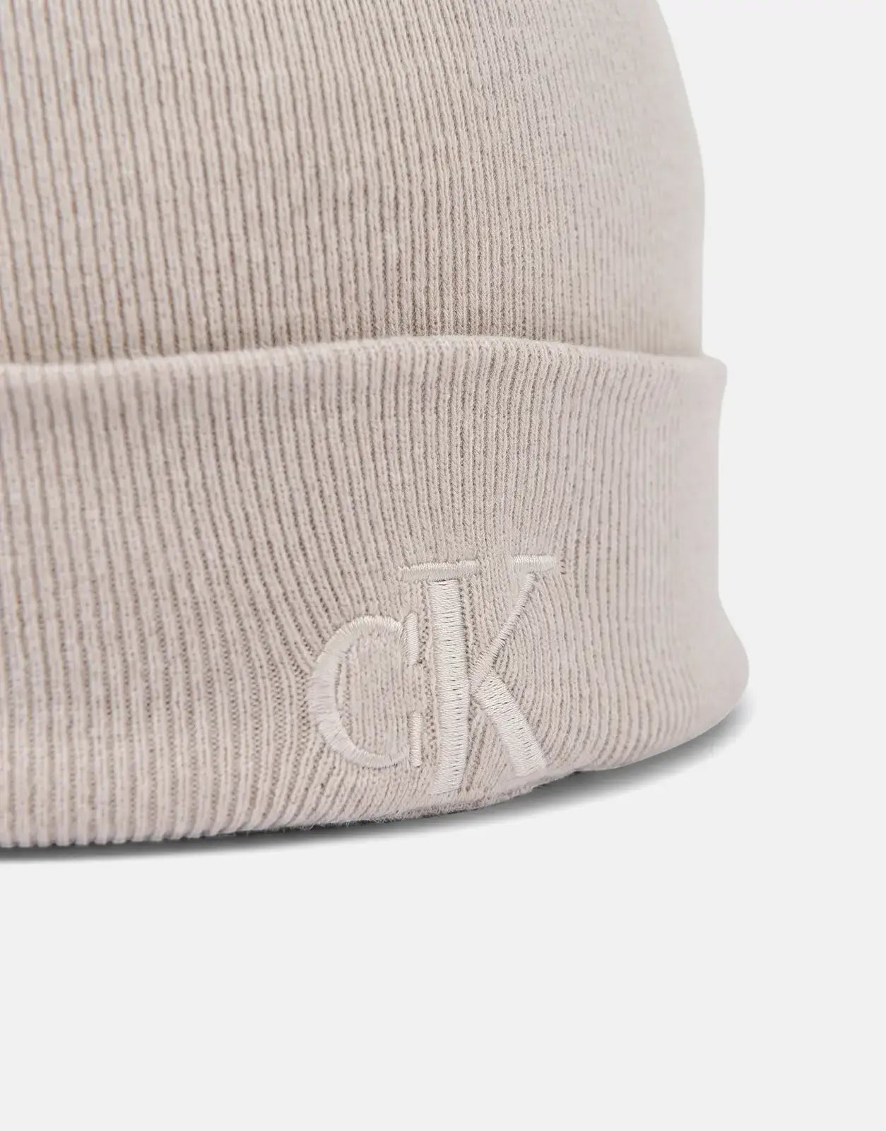 Close-up of a Calvin Klein Fine Rib Beige Beanie, showcasing the ribbed knit texture and embroidered CK logo on the folded