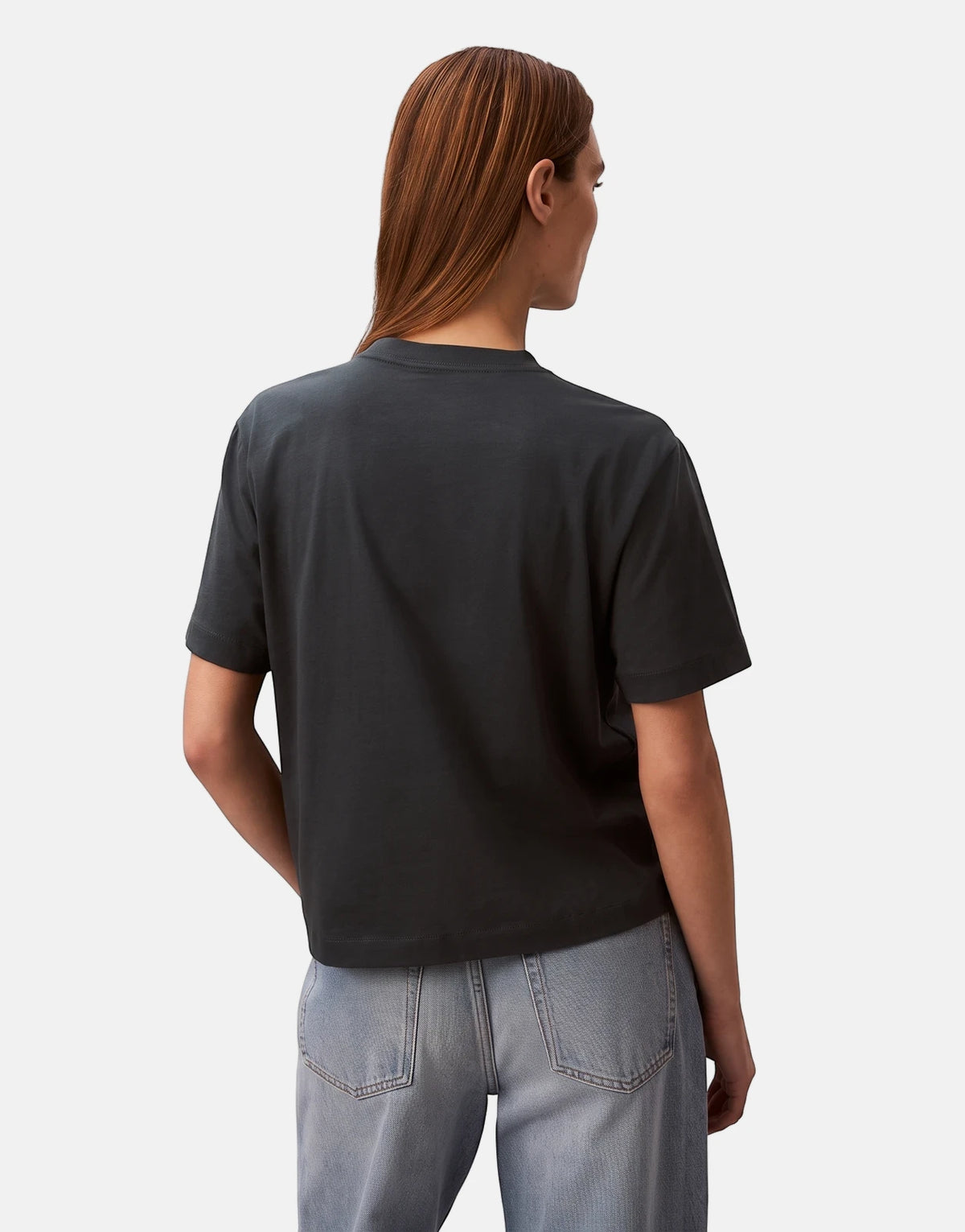 Female model wearing a Calvin Klein Graphic Boxy Navy T-Shirt and light wash jeans, viewed from the back.