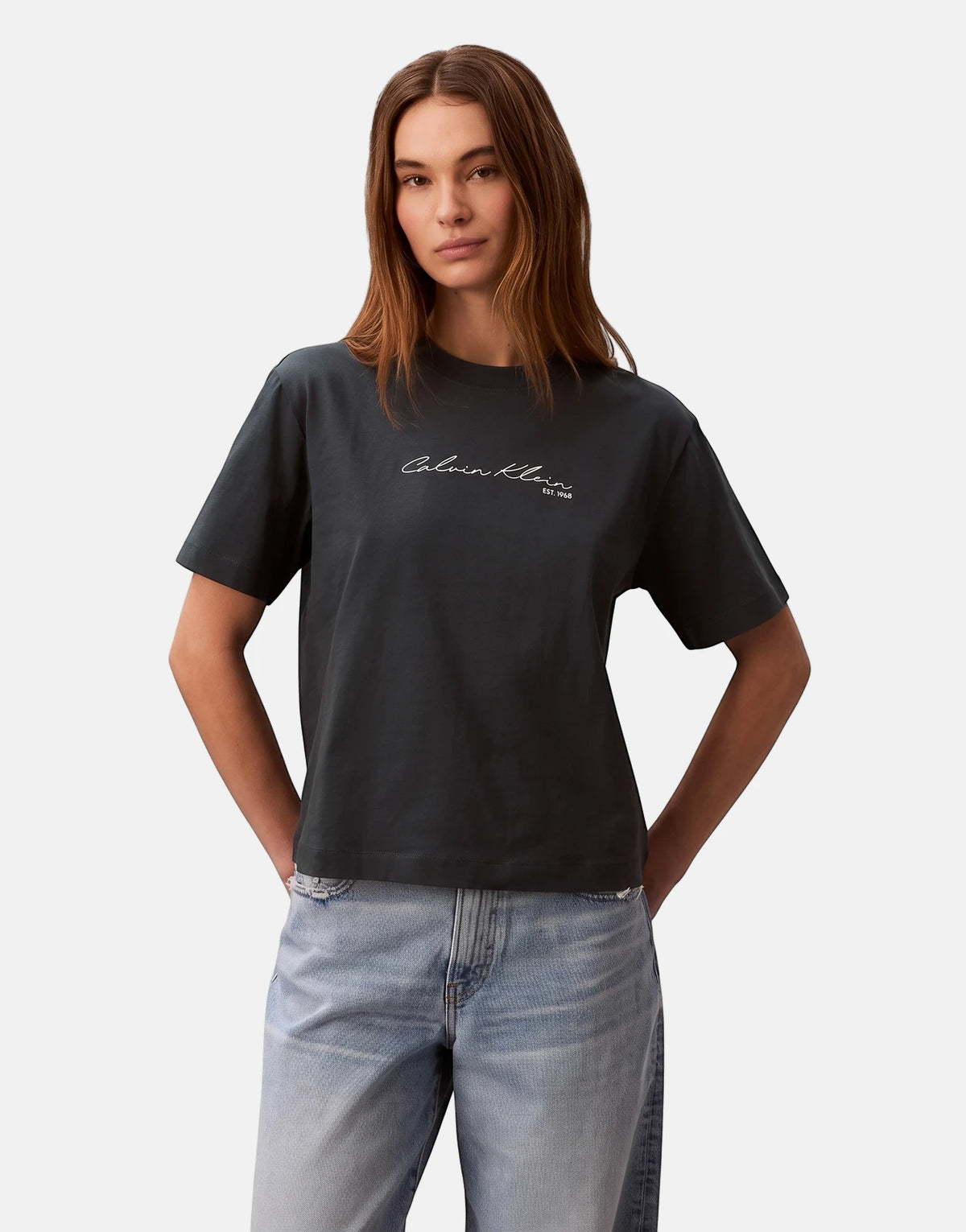 Female model wearing a Calvin Klein Graphic Boxy Navy T-Shirt and light wash jeans, showcasing the shirt's fit and logo.