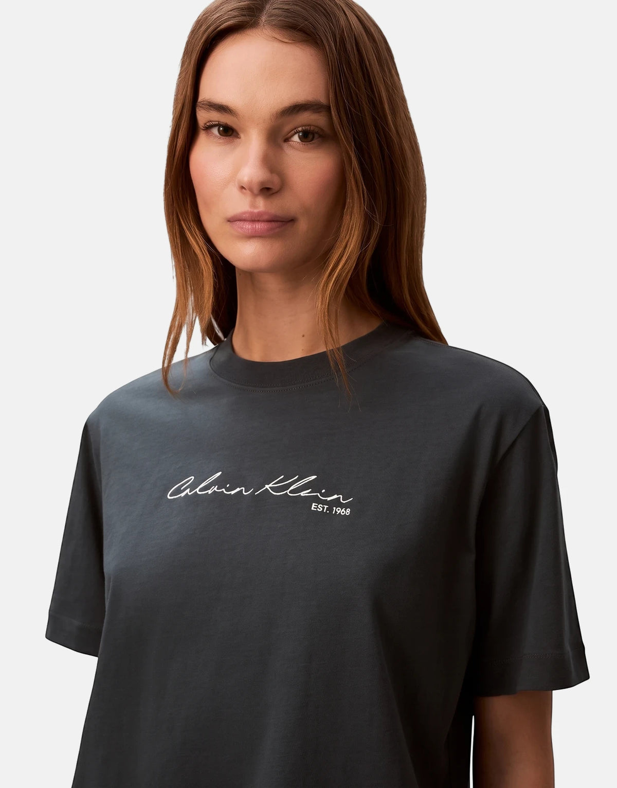 Model wearing a dark navy Calvin Klein graphic boxy t-shirt with a white script logo on the chest, studio shot.