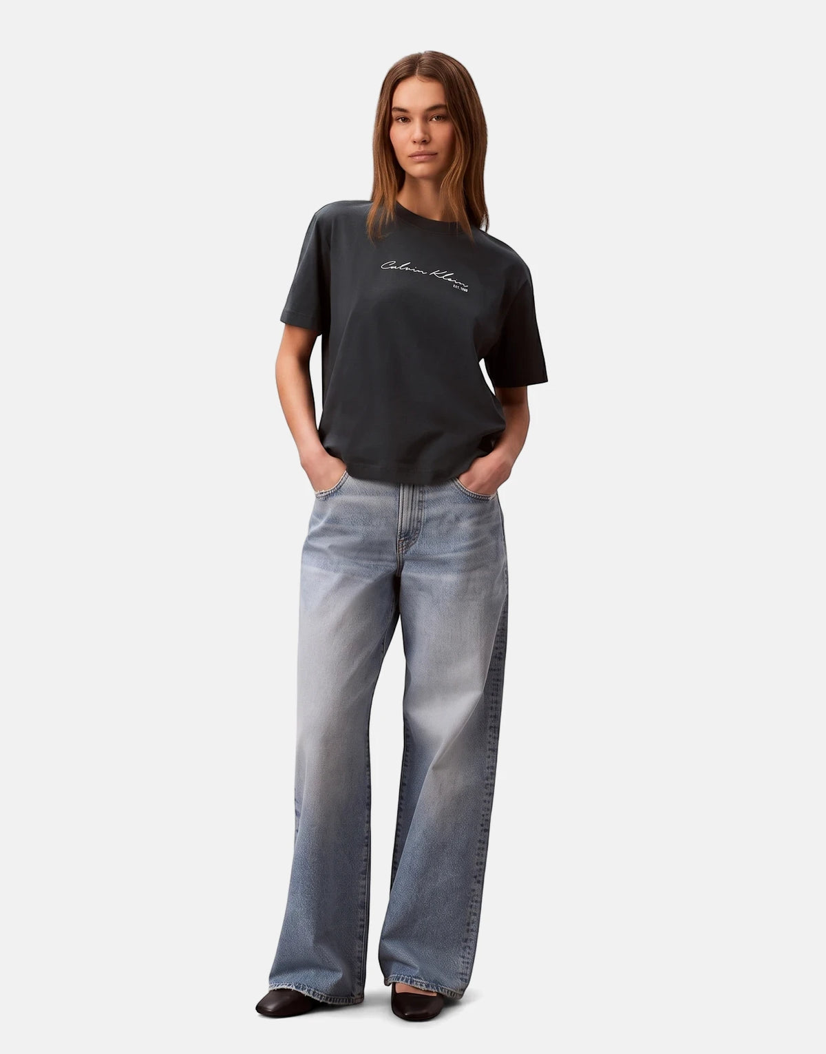 Full-body shot of a woman wearing a navy Calvin Klein graphic boxy t-shirt with a white logo and light blue wide-leg jeans.