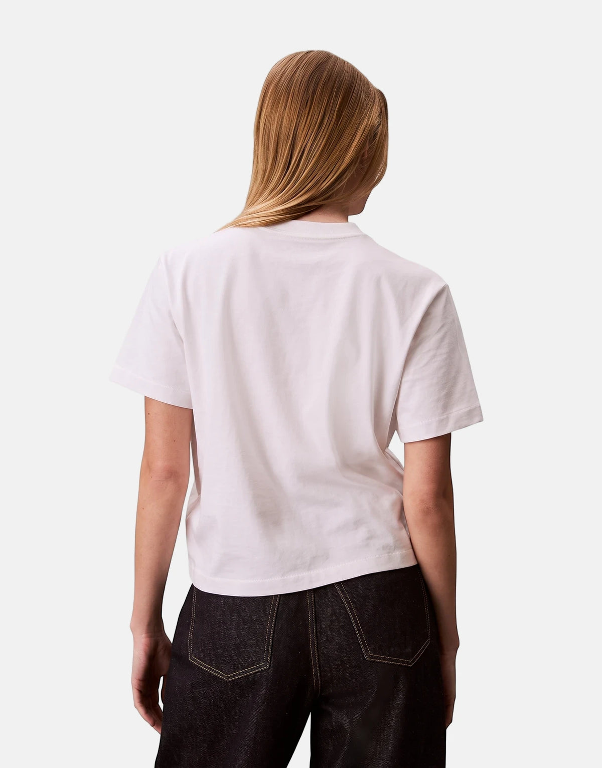 Female model from the back wearing a Calvin Klein Graphic Boxy White T-Shirt with dark jeans.