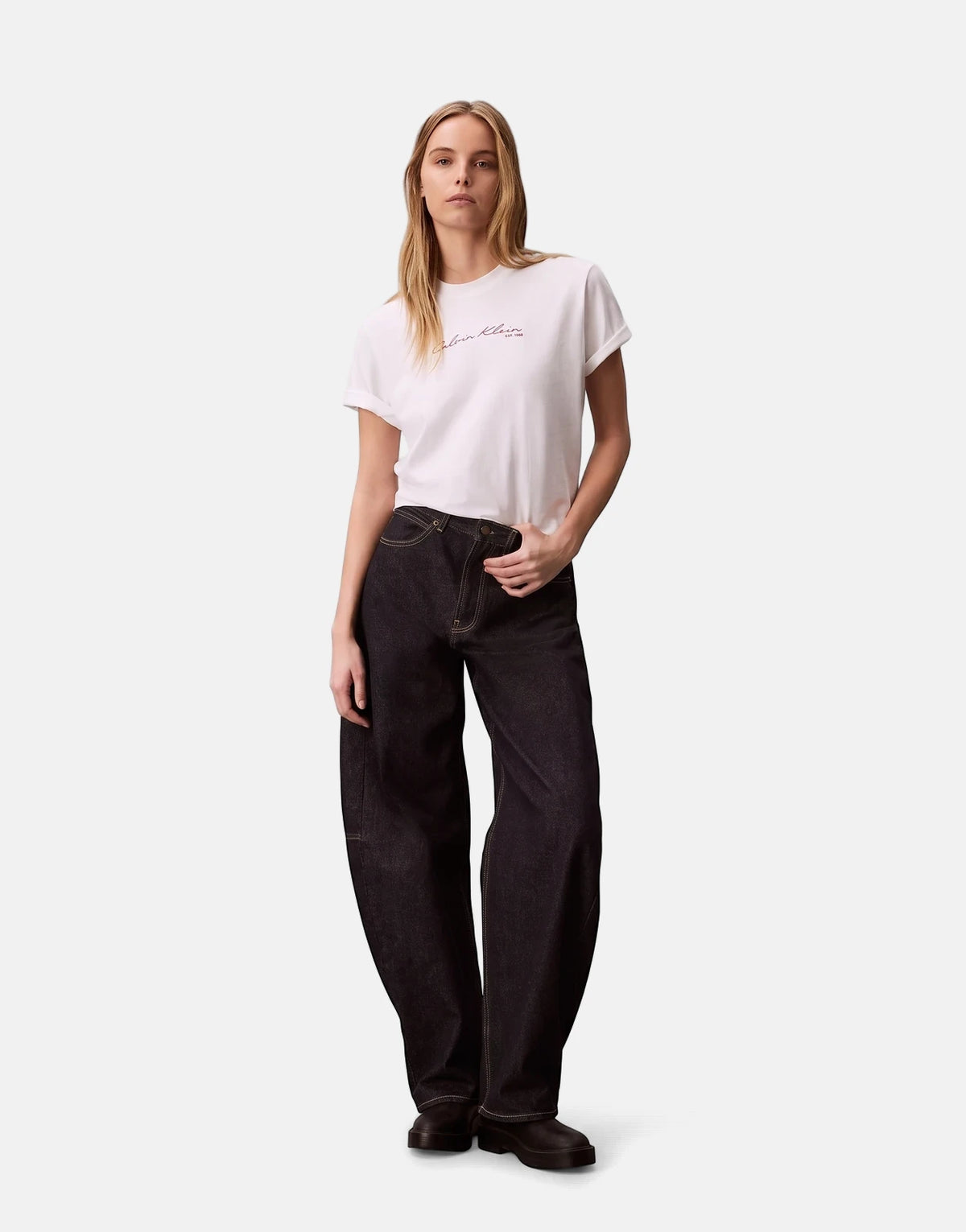 Female model wearing a Calvin Klein Graphic Boxy White T-Shirt and dark wash wide-leg jeans, posing full body.