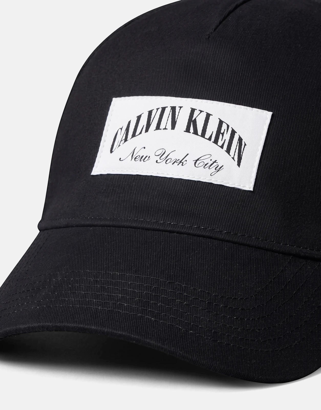 Black Calvin Klein Heritage Crest cap with a white logo patch, made of durable fabric, shown in a close-up view.