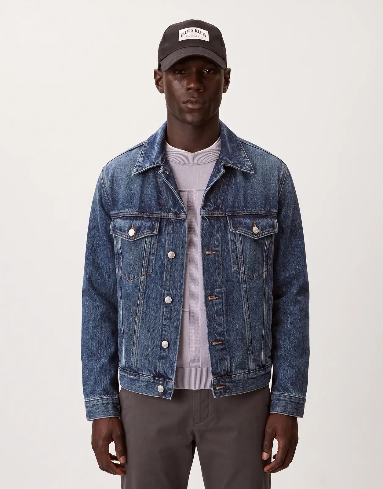 A man wearing a black Calvin Klein Heritage Crest baseball cap with a white patch logo and a blue denim jacket.