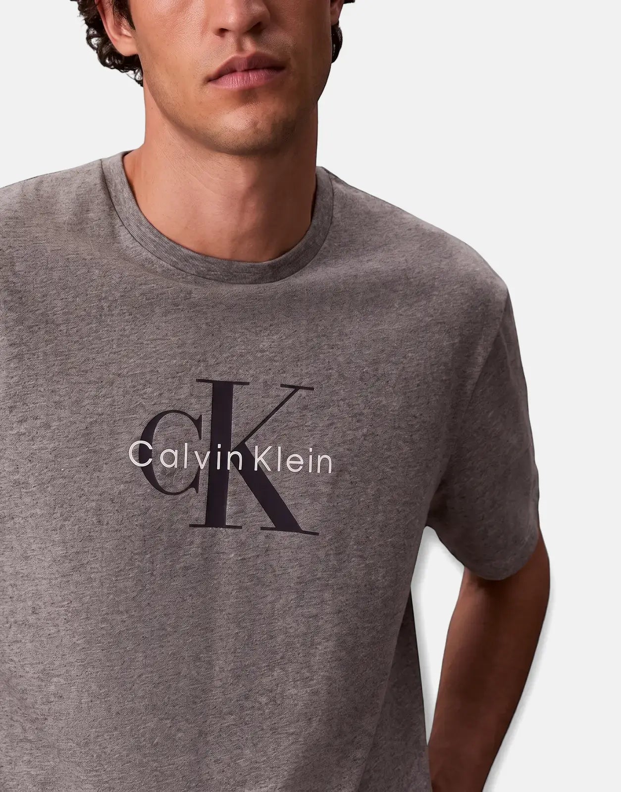 Close-up of a man wearing a grey Calvin Klein Hero Monologo T-shirt with the brand's logo prominently displayed on the chest.