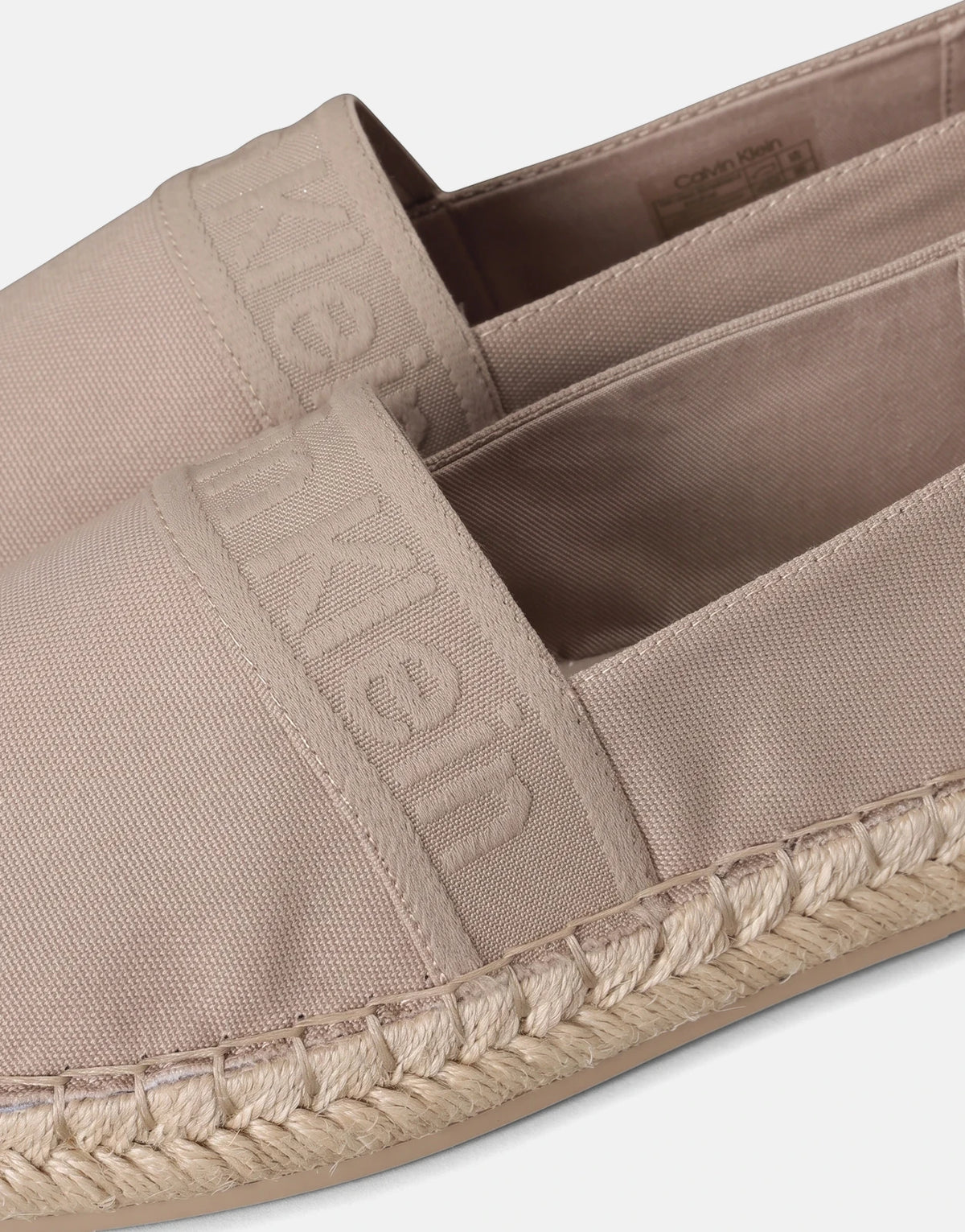 Two light brown Calvin Klein Oblique espadrille slip-on shoes with canvas uppers and braided jute soles, in a close-up view.