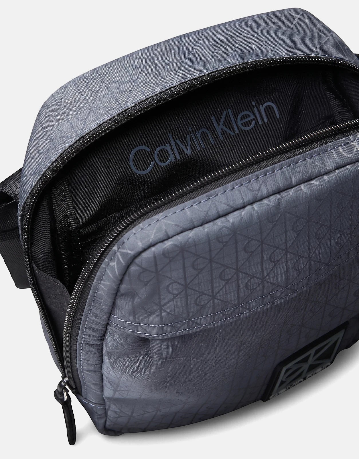 Close-up of a blue-grey Calvin Klein Utility Emblem Reporter Bag made from textured fabric, featuring a top zipper opening