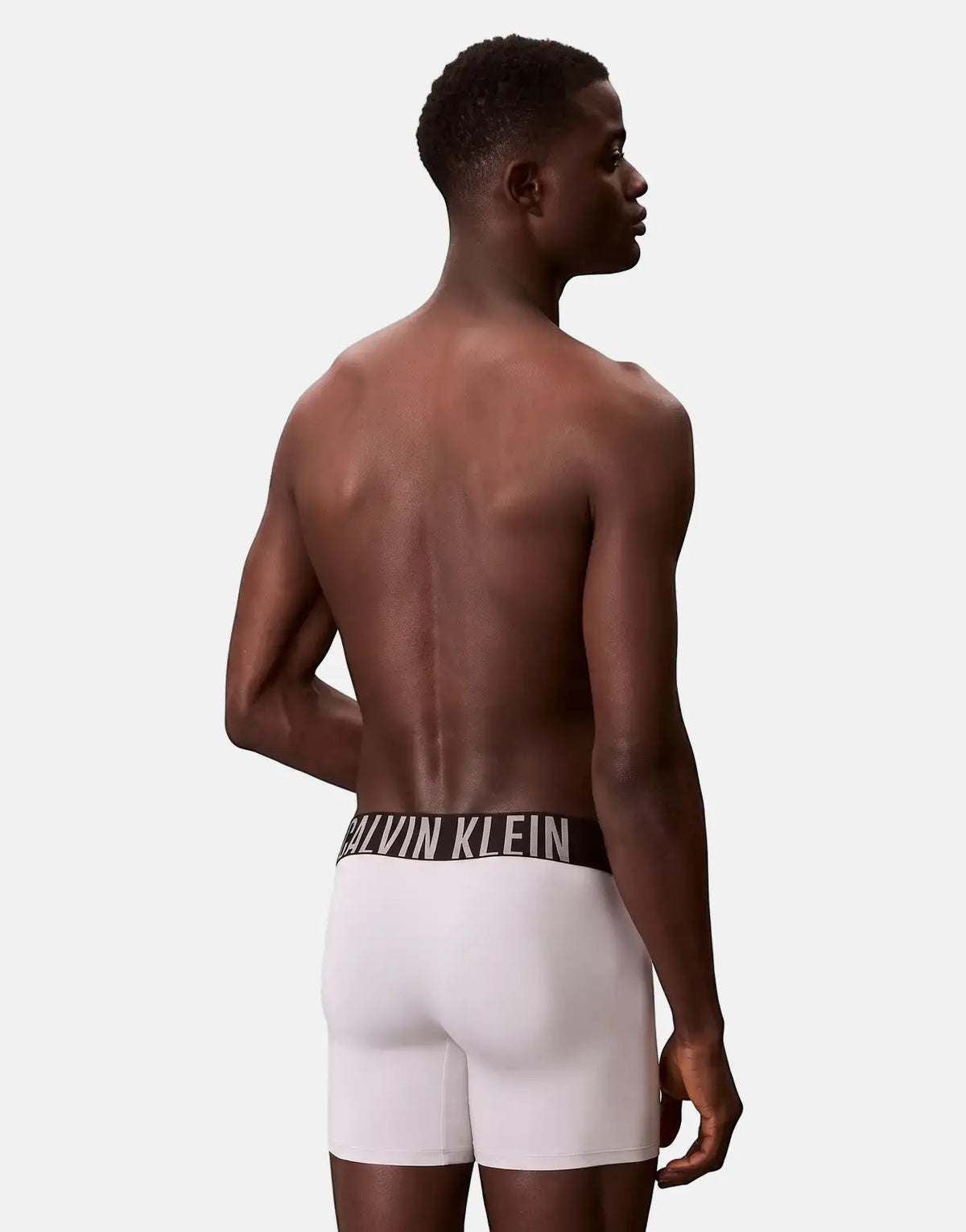 Male model wearing white Calvin Klein boxer briefs, showcasing the iconic logo waistband from a back view.