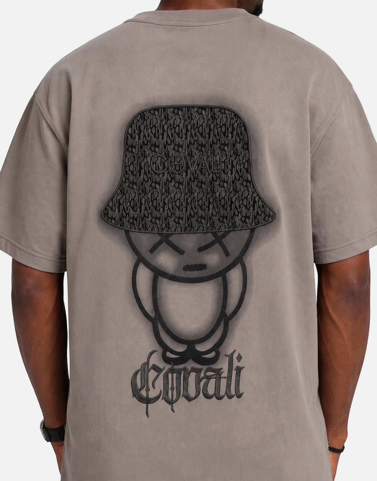 Back view of a person wearing an oversized Covali Punto Grey T-Shirt featuring a black graphic of a bucket hat and character