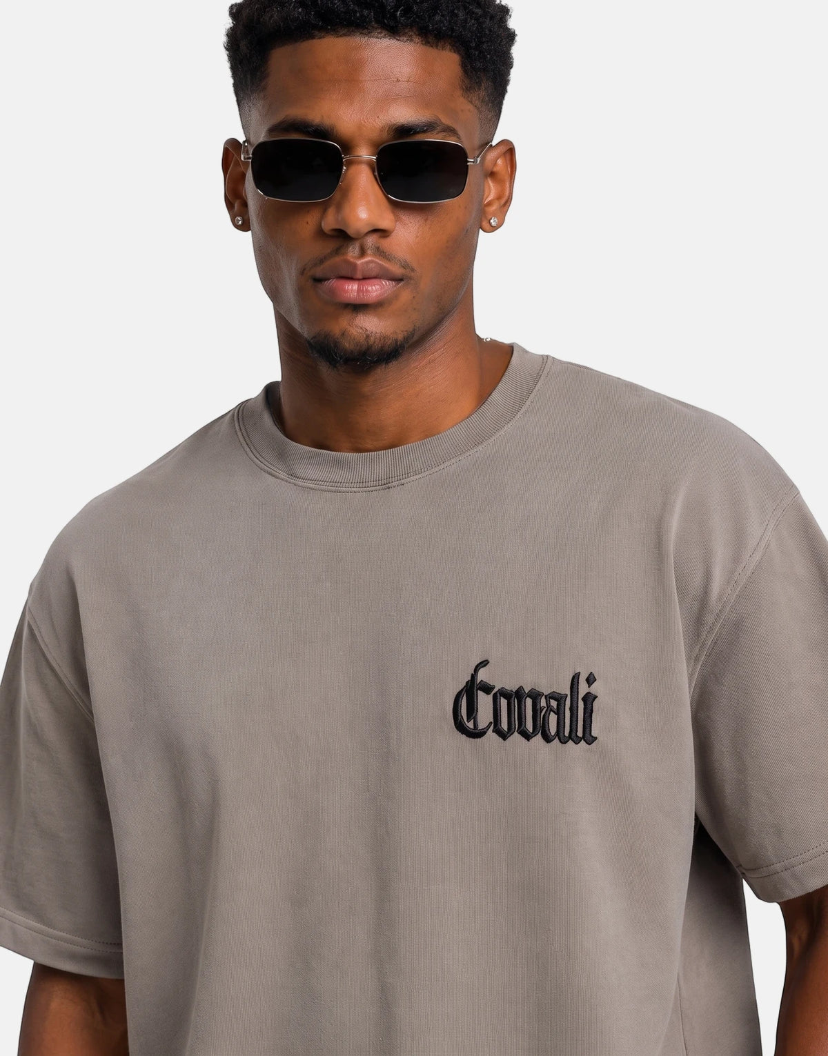 Close-up of a man wearing a grey Covali Punto T-Shirt with a black embroidered logo, accessorized with rectangular