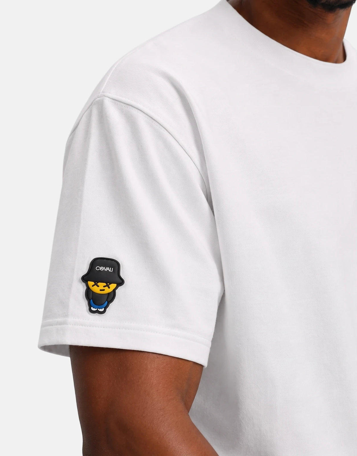 Close-up of a person wearing a white Covali Tipo T-Shirt with a unique black and yellow cartoon character patch on the