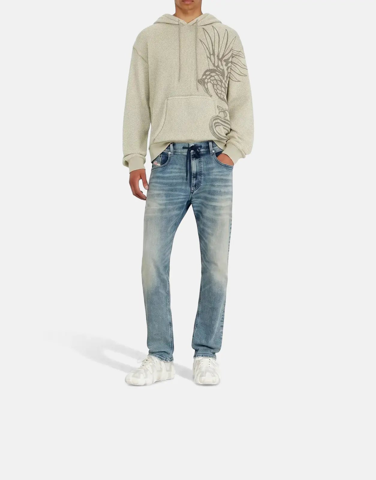 Male model in a light beige waffle-knit hoodie, light blue Diesel 2032 D-Krooley B Jogger jeans, and a distressed cap.