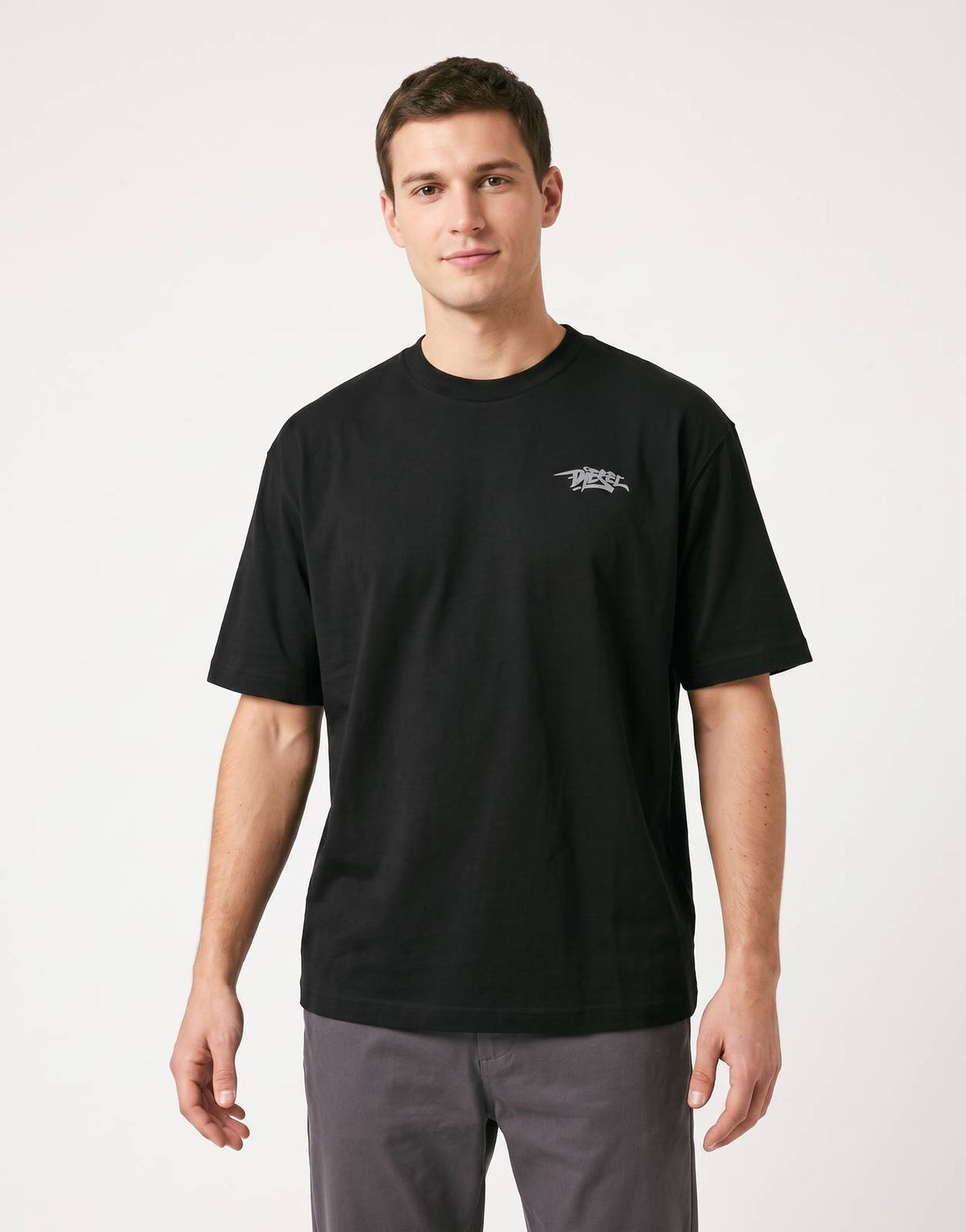 Man wearing a black Diesel T-Boggy V5 T-Shirt 9XX with a grey logo. The model is paired with neutral grey pants on a white