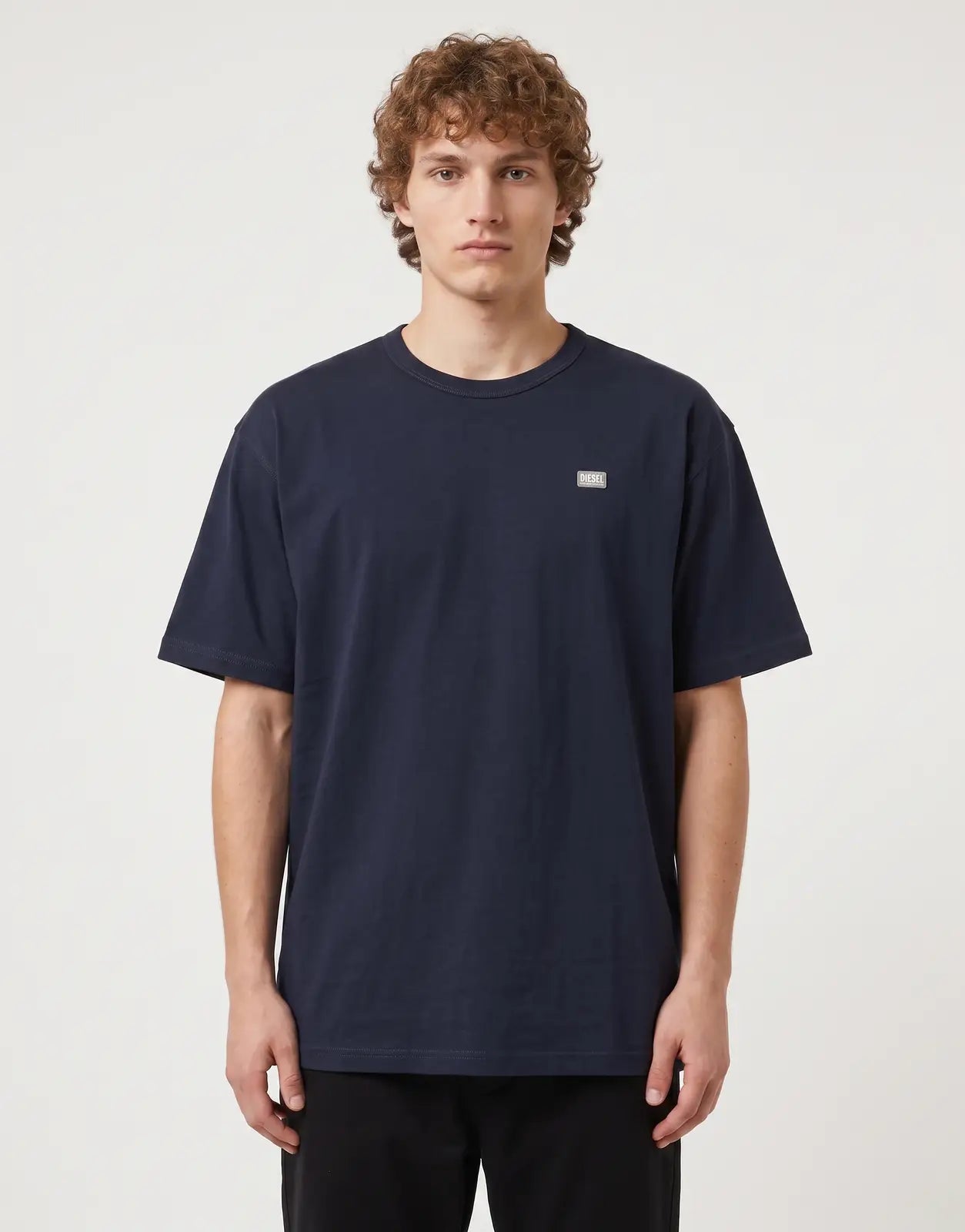 A male model wears a navy blue Diesel T-Boxt R30 Relaxed 81E T-Shirt with a subtle Diesel logo on the chest, standing