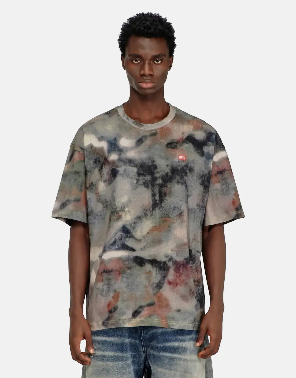 Male model wears Diesel T-Boxt V7 t-shirt 8ATA with a multi-colored abstract pattern and blue jeans.