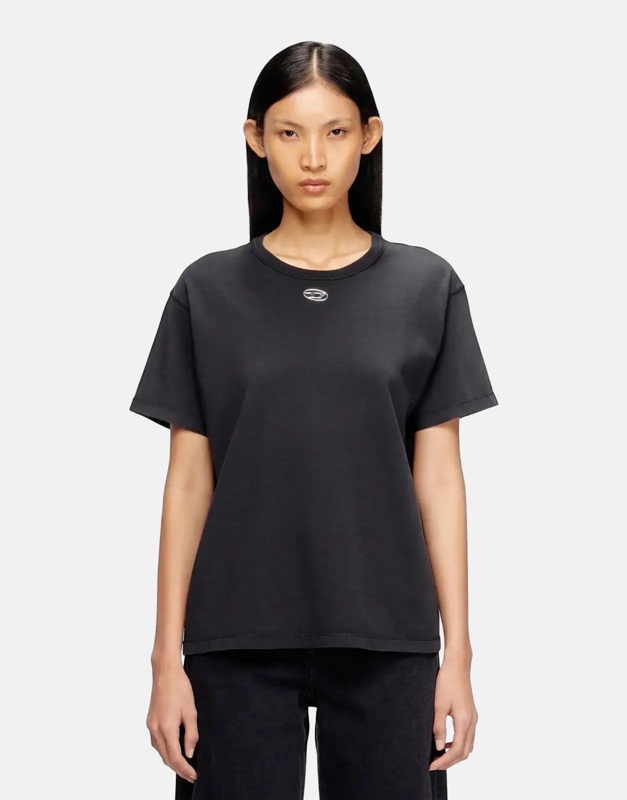 An Asian female model wearing a black Diesel T-Normy OD S1 Regular T-Shirt with a silver oval logo, paired with black jeans,