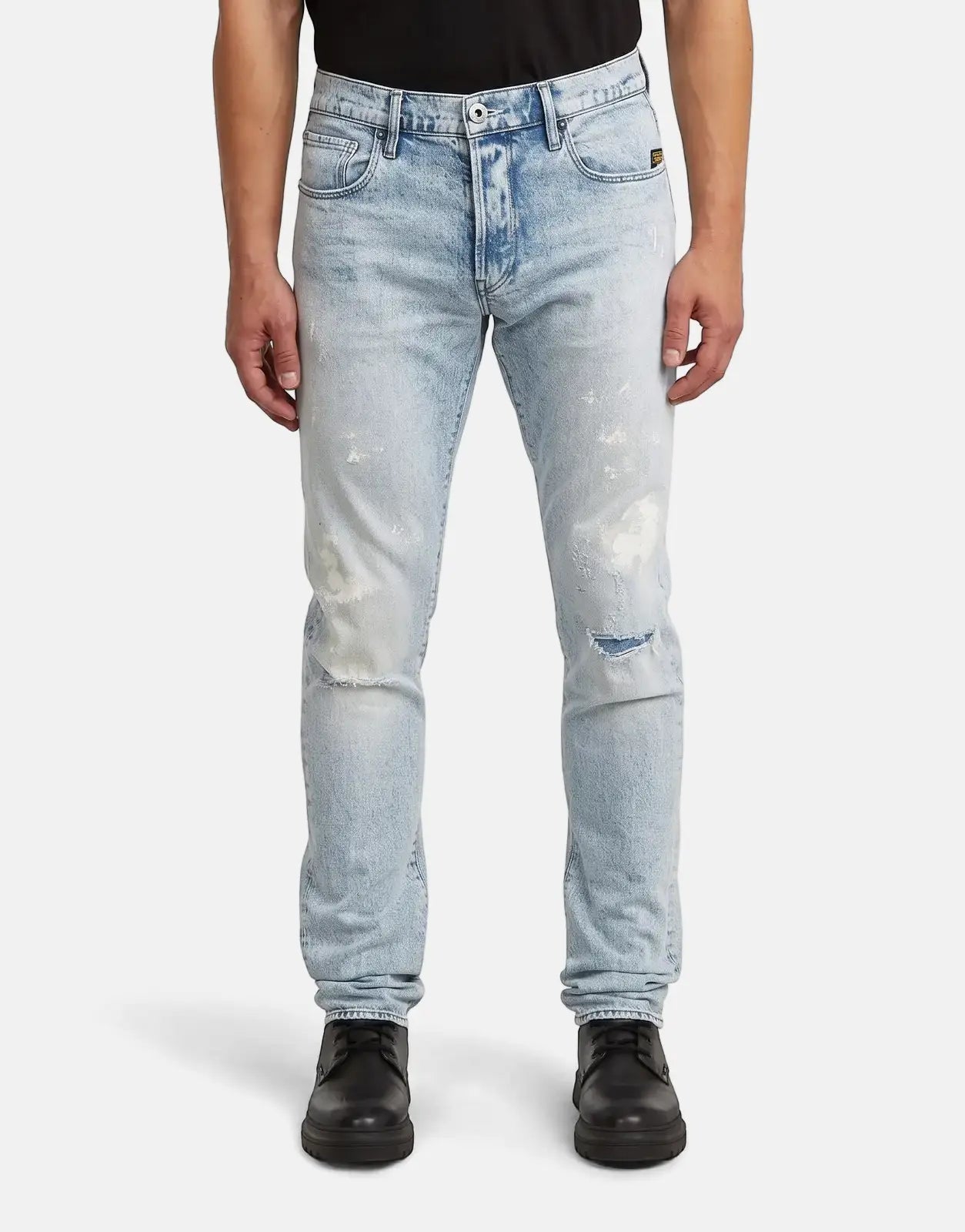 A man models G-Star RAW 3301 Slim Sun Faded Paint Blue jeans, featuring light blue distressed denim with white paint
