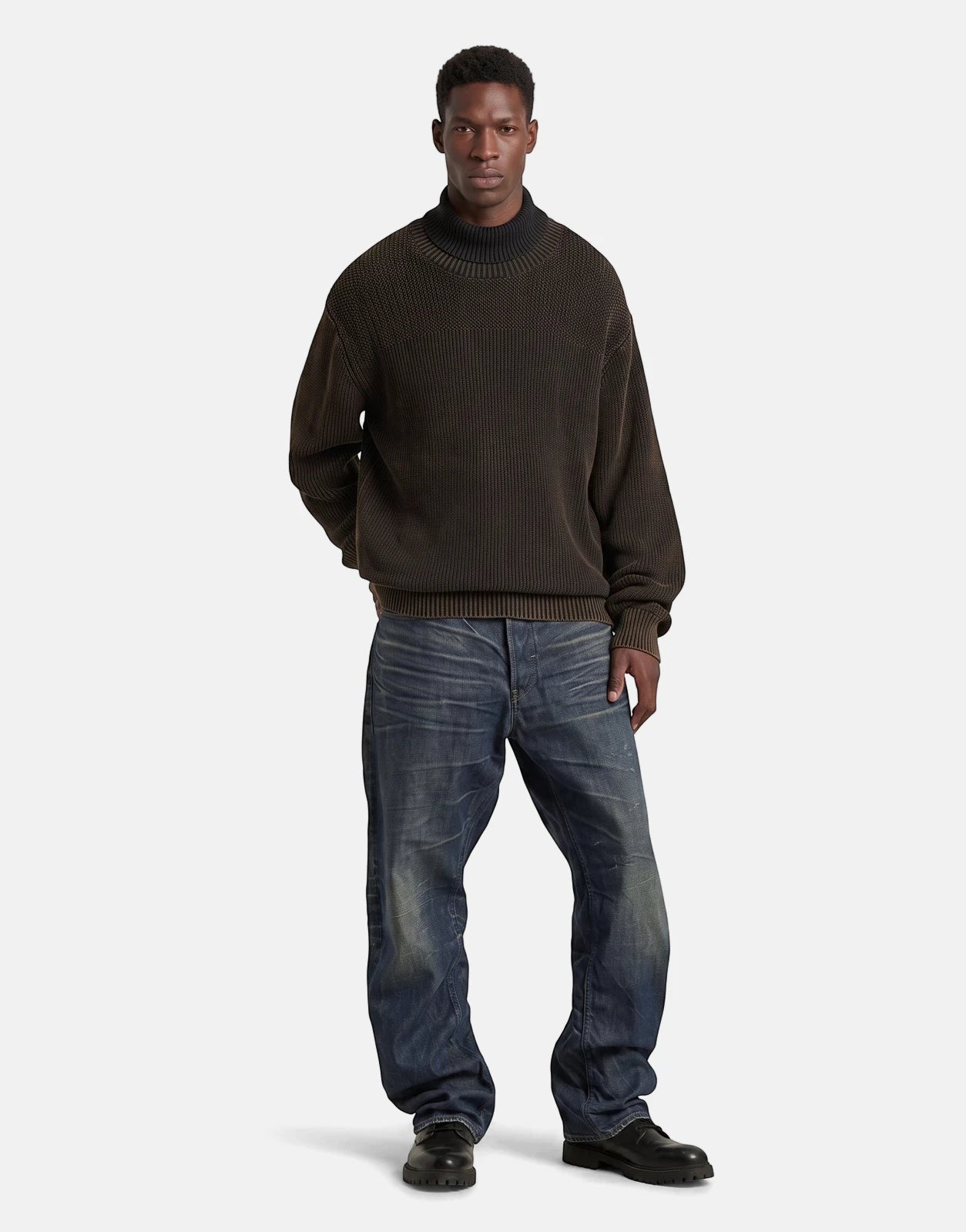 Male model wearing G-Star RAW Arc 3D Loose Raw Vintage Jeans in blue, paired with a dark brown chunky knit turtleneck