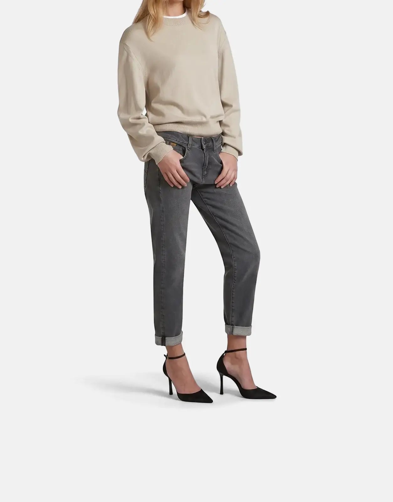 Blonde model wearing a beige G-Star RAW Boxy Knit Brick sweater, dark grey cuffed jeans, and black high heels in a full body