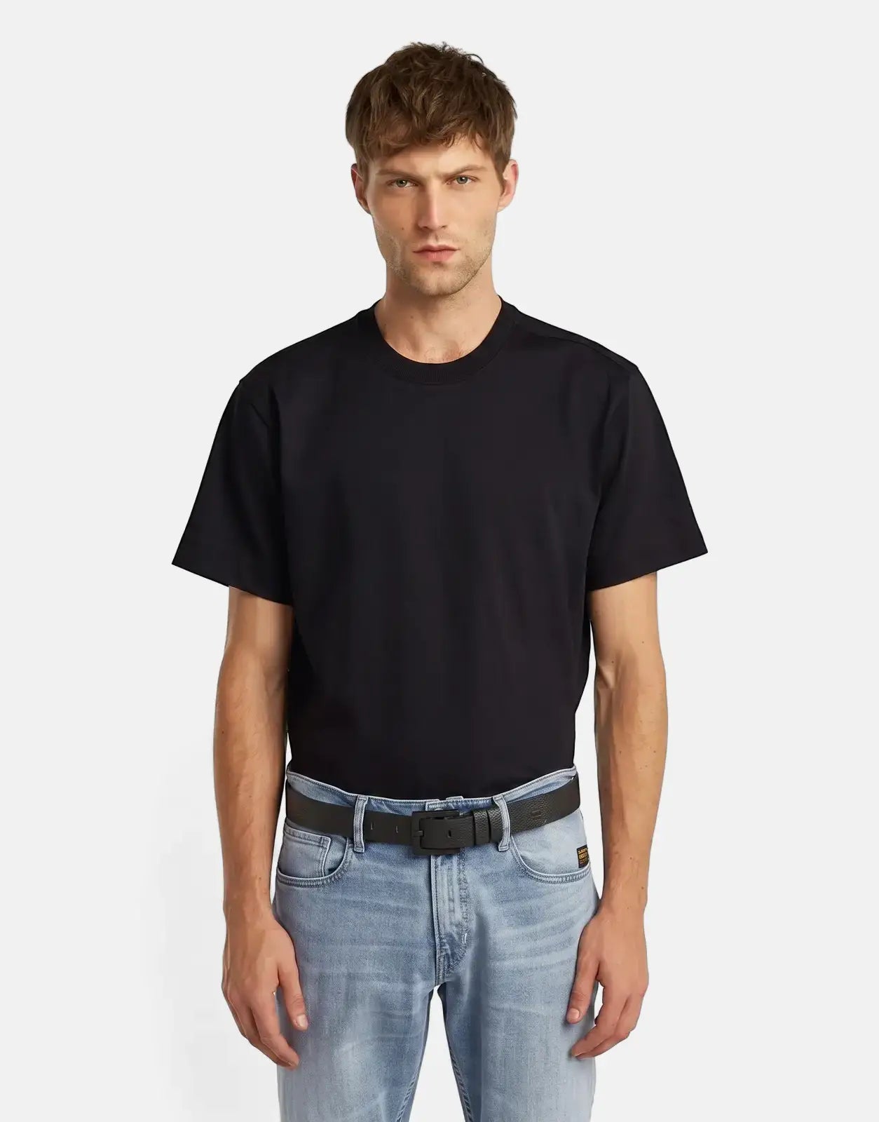 Man wearing a black G-Star RAW Duko belt with a black buckle, styled with a black t-shirt and light blue jeans, standing