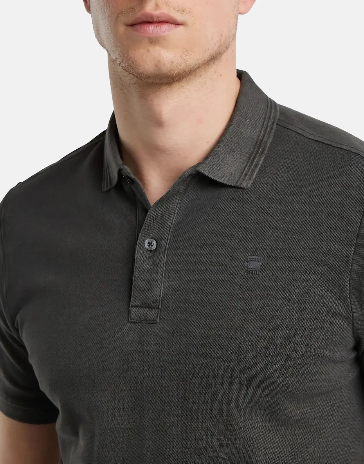 Close-up of a man wearing a G-Star RAW Dunda Overdyed Black Slim Polo Shirt, showcasing the dark gray color and knit texture.