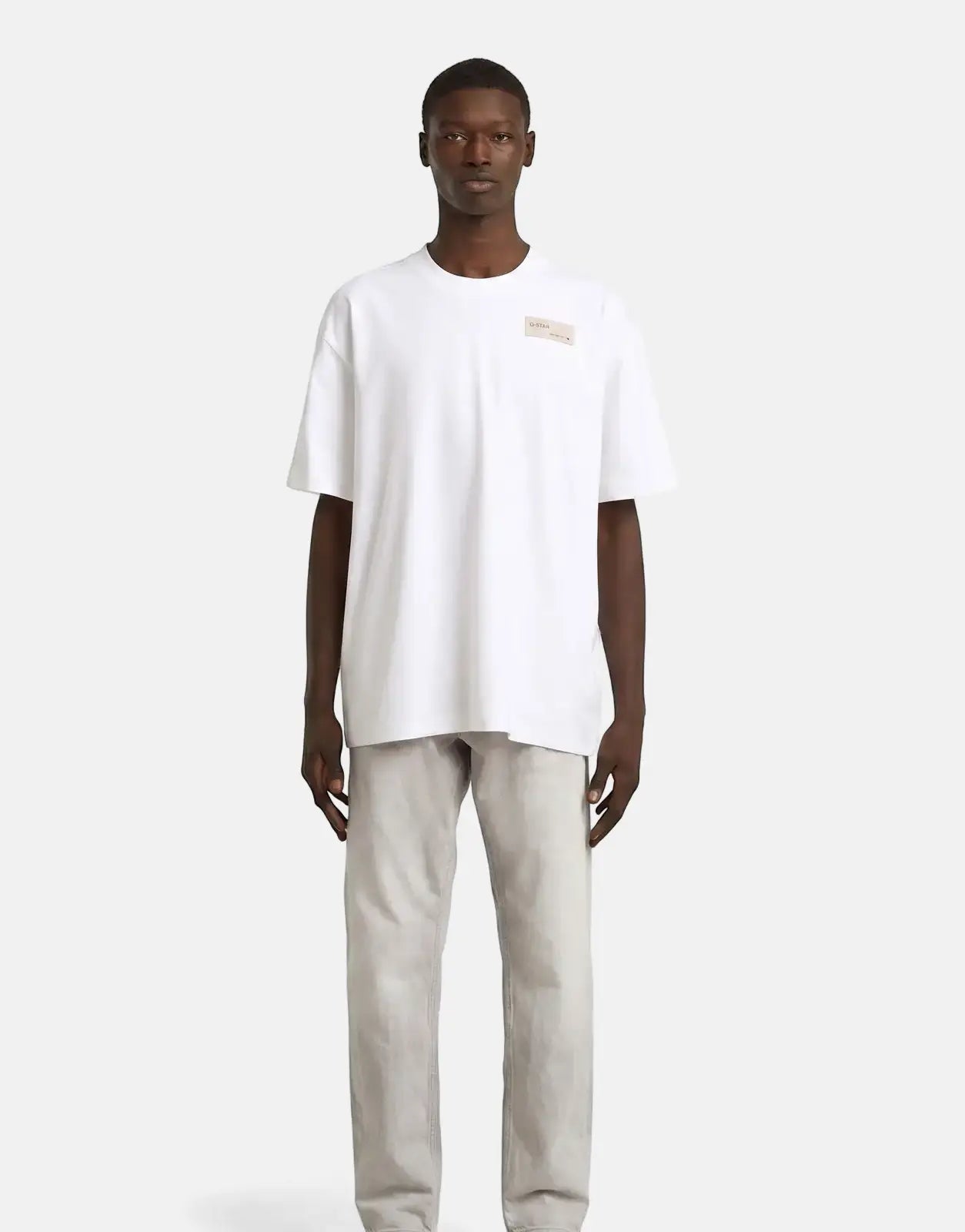 Male model wearing a G-Star RAW HB Badge Relaxed White T-Shirt with short sleeves and light gray pants.